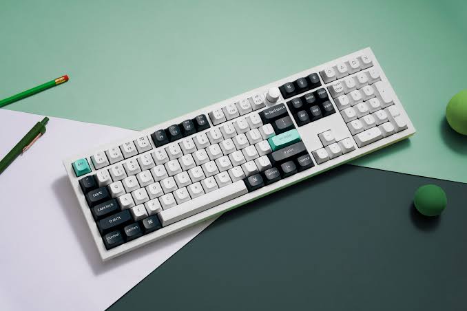 White mechanical keyboard with black and teal keycaps on a minimalist desk setup.