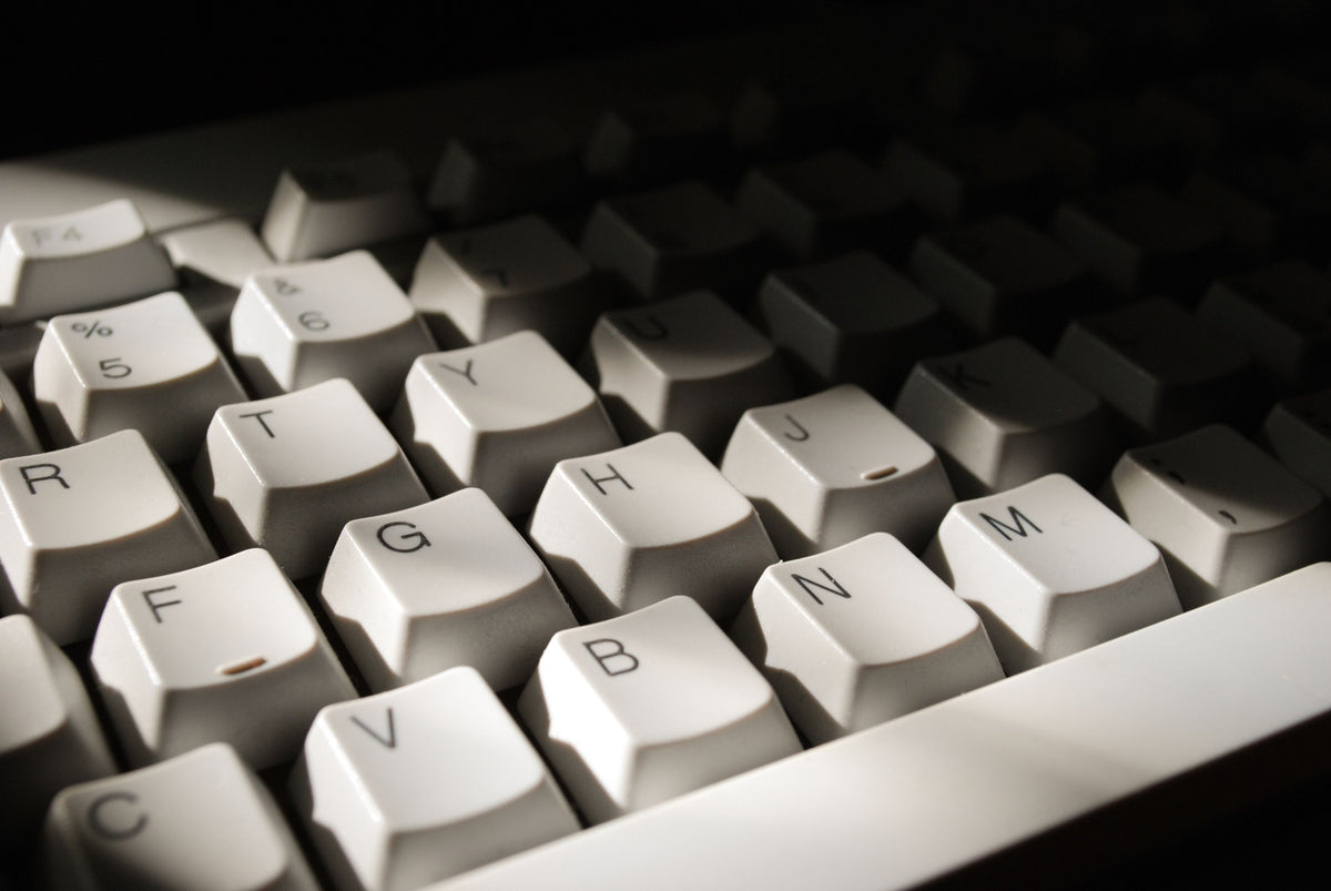 Close-up of a white mechanical keyboard with partially legible keys under dramatic, low-key lighting.